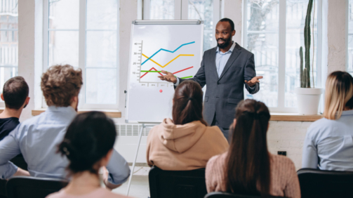 Explaining. Male speaker giving presentation in hall at university workshop. Audience or conference hall. Rear view of unrecognized participants. Scientific, business event, training. Education